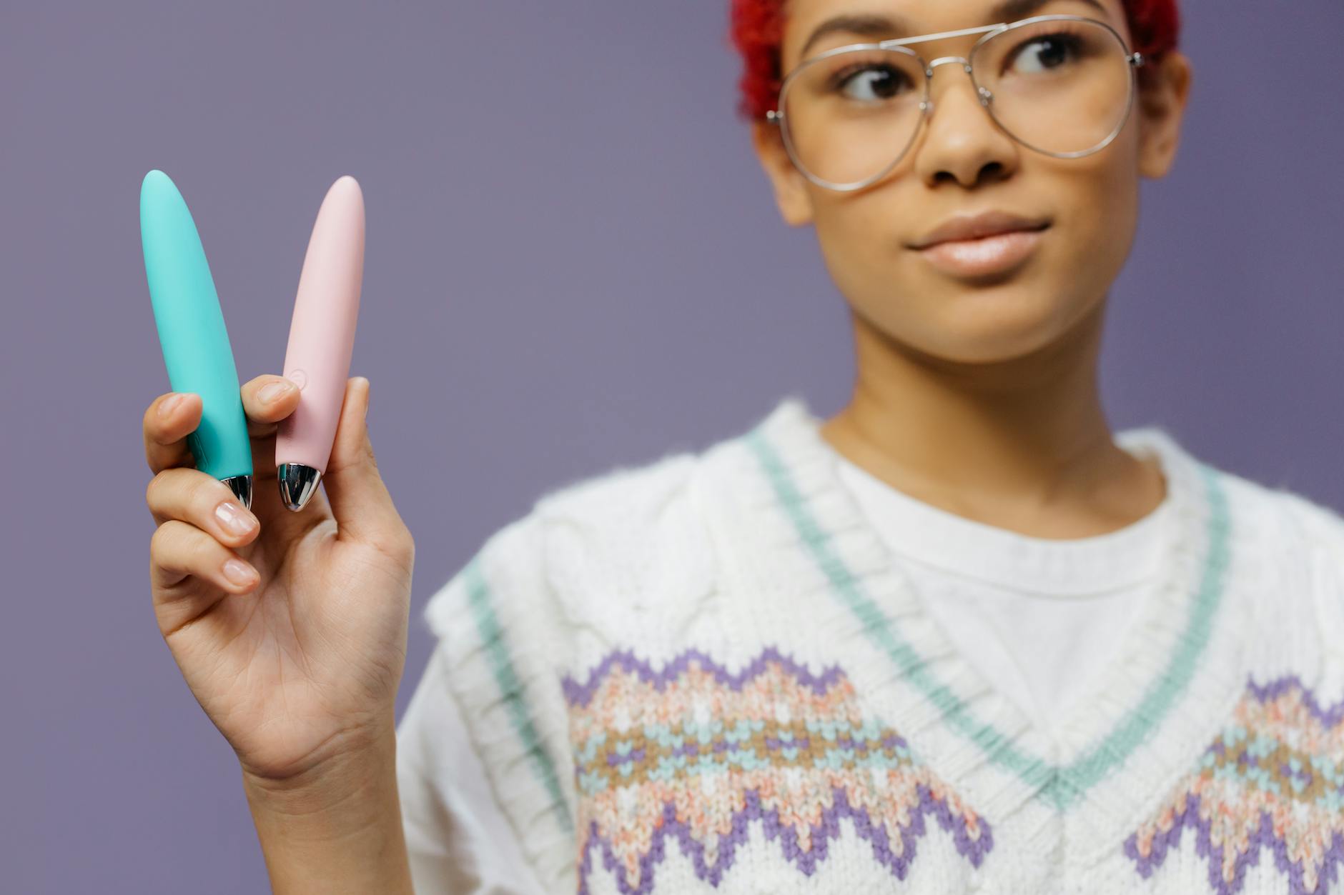 A woman holding two colorful vibrators against a purple background