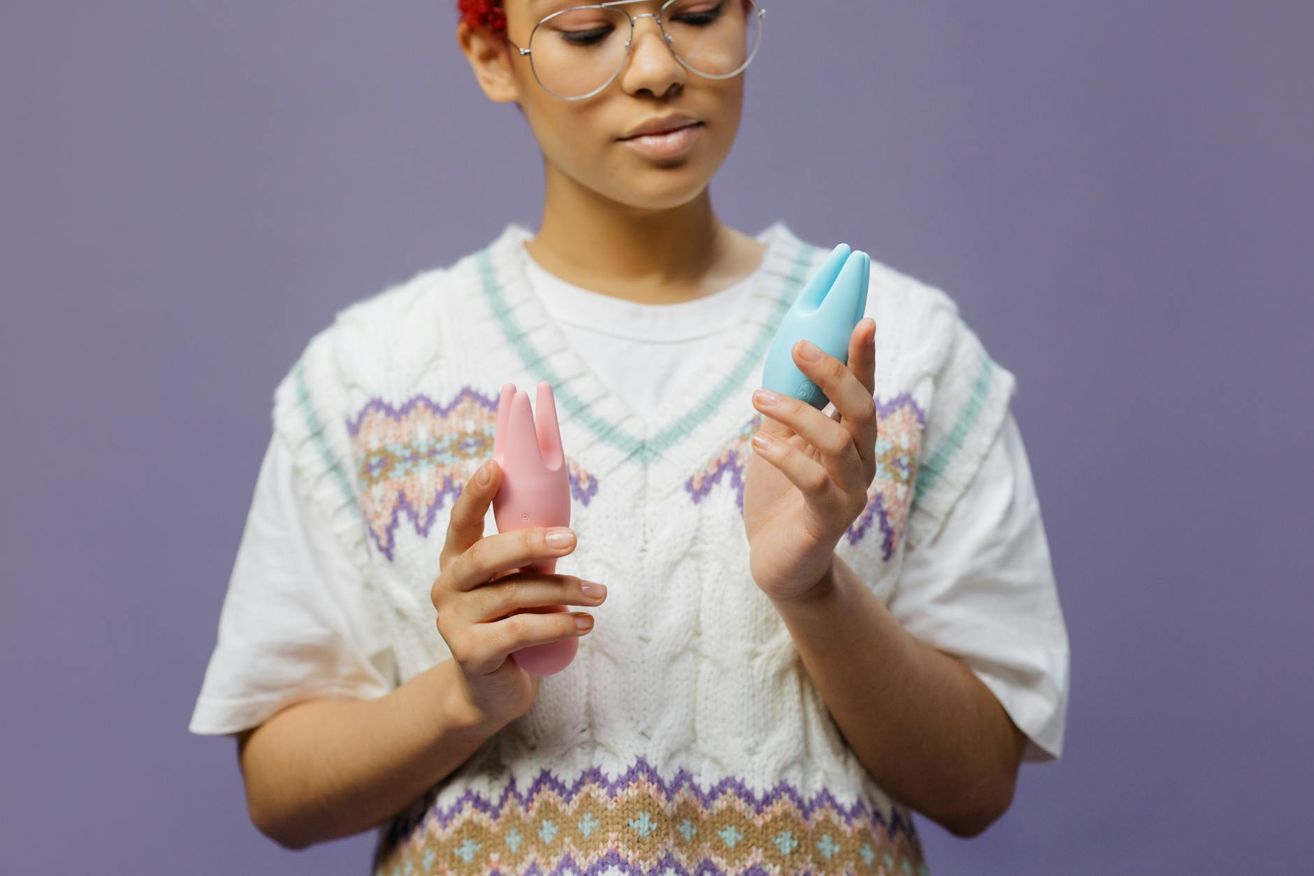 Woman holding a pink silicone clitoral vibrator in both hands, looking thoughtful.