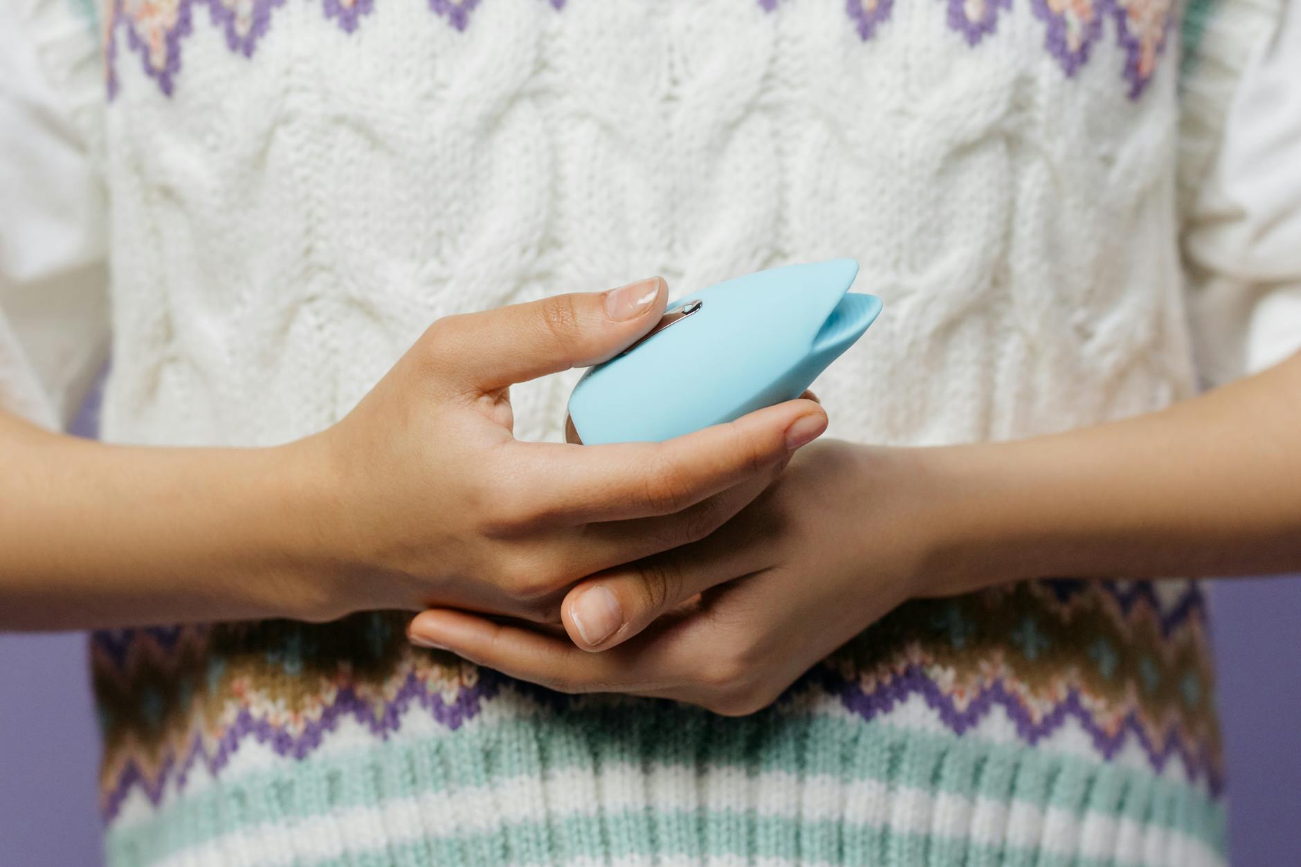 Close-up of hands holding a lemon vibrator against a knitted sweater during intimate time together.